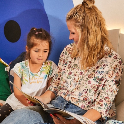 kita-kinderzimmer-hamburg-startseite Frau ließt Kind ein Buch vor.