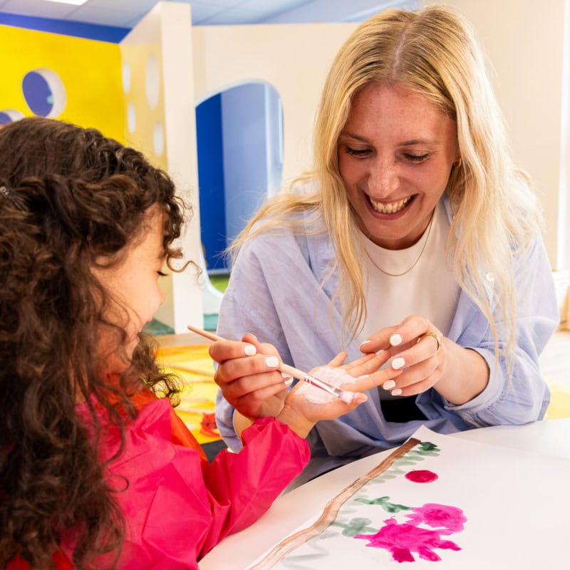 Pädagogin die einem Kind Fingerfarbe aufrägt in der Kita kinderzimmer Hamburg