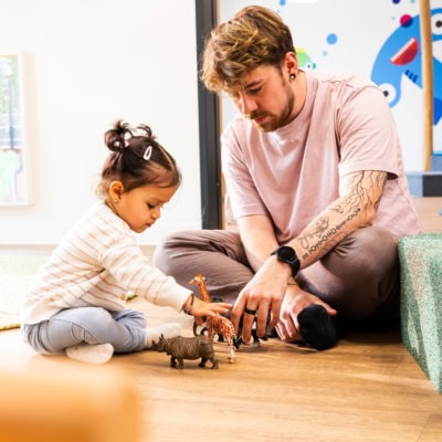 kita-kinderzimmer-hamburg-brand-shooting-kjell-madchen-3x7a3898 Ein Erzieher spielt zusammen mit einem Kind mit Zoofiguren in der Kita kinderzimmer Hamburg