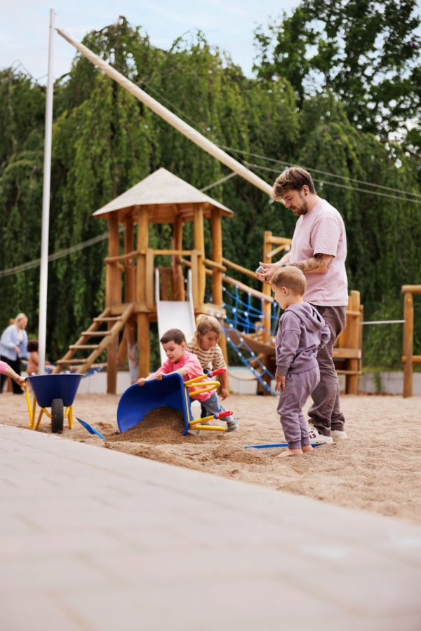kita-kinderzimmer-hamburg-brand-kjell-kinder-draußen-spielen Pädagoge spielt mit vielen Kindern auf Spielplatz