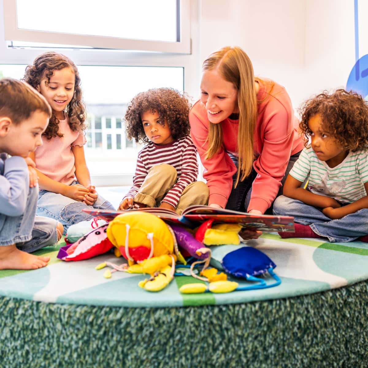 vorschule-kita-kinderzimmer-hamburg-kita-motiv-3X7A4598 Eine Erzieherin liest mit einer Gruppe Kinder in einem Buch in der Kita kinderzimmer Hamburg